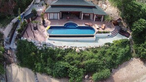 Una casa grande con piscina, rodeada de abundante vegetación y un paisaje montañoso.