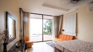 Un dormitorio moderno con una cama grande, un sofá naranja, una mesa de comedor y vistas a una piscina.