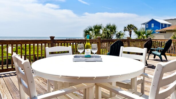 A round white table with two wine glasses and a bottle on a wooden deck overlooking the ocean. - East End Escape | Ocean Views, Spacious Deck & Quiet Beach Area Near Public Access (Folly Beach)