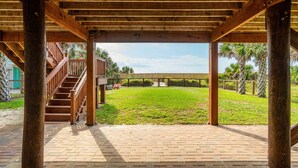 A covered outdoor area with a brick floor, wooden pillars, and a staircase leading to a higher level. - East End Escape | Ocean Views, Spacious Deck & Quiet Beach Area Near Public Access (Folly Beach)