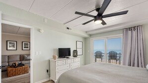 Quarto com cama grande, ventoinha no teto, cômoda e televisão. Tem vista para o mar pela janela.