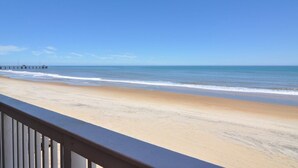 Uma praia com um corrimão de madeira, um cais ao longe e céus azuis cristalinos.