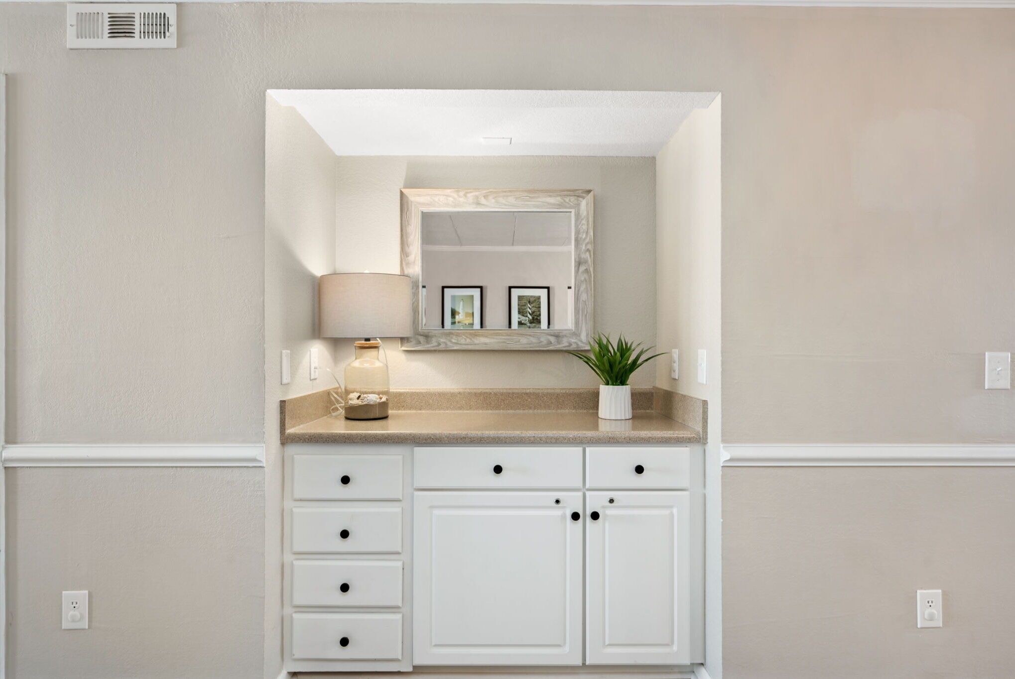 A bathroom with a vanity, a mirror, a lamp, and a potted plant.
