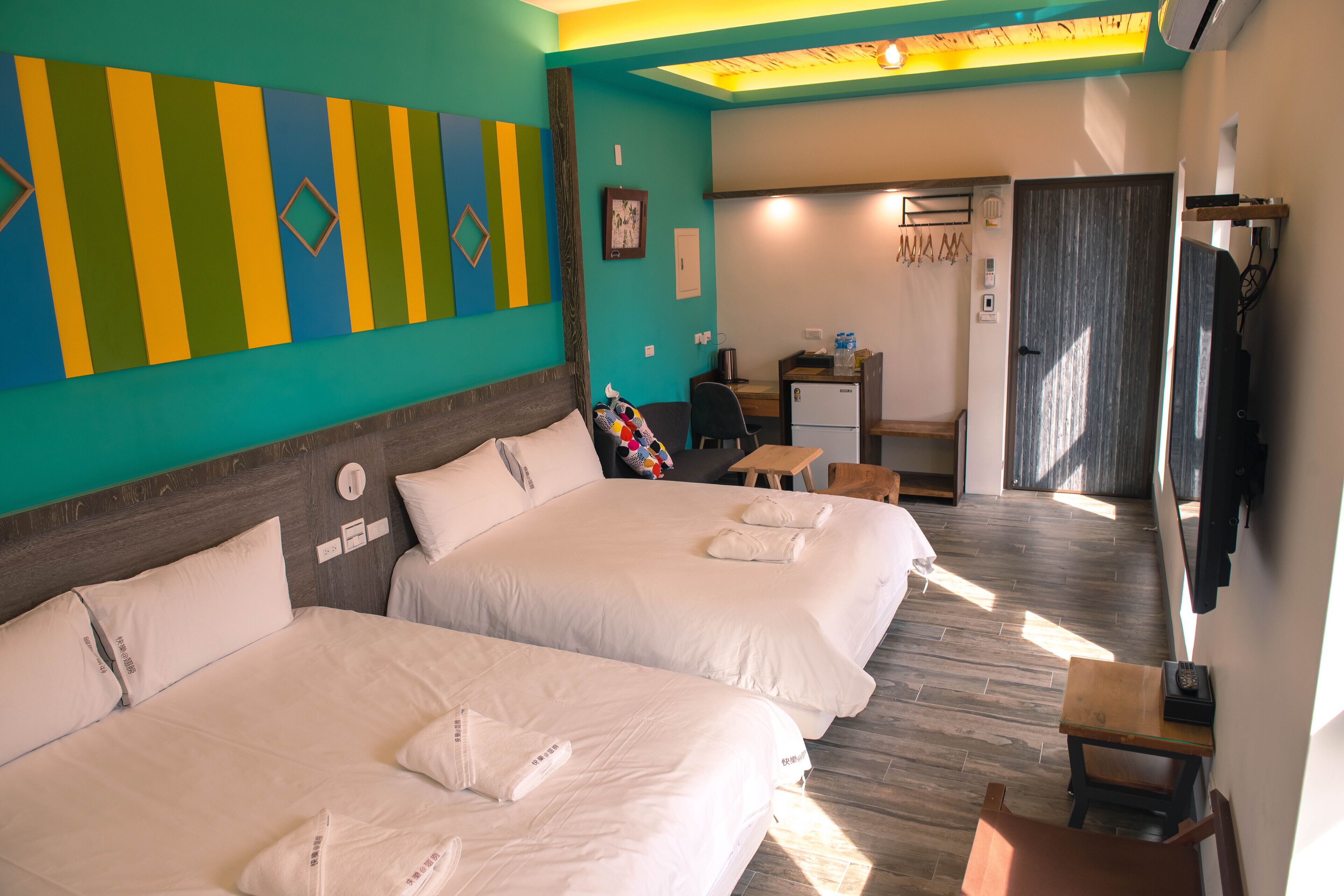 A hotel room with two beds, a desk, a chair, and a small table.