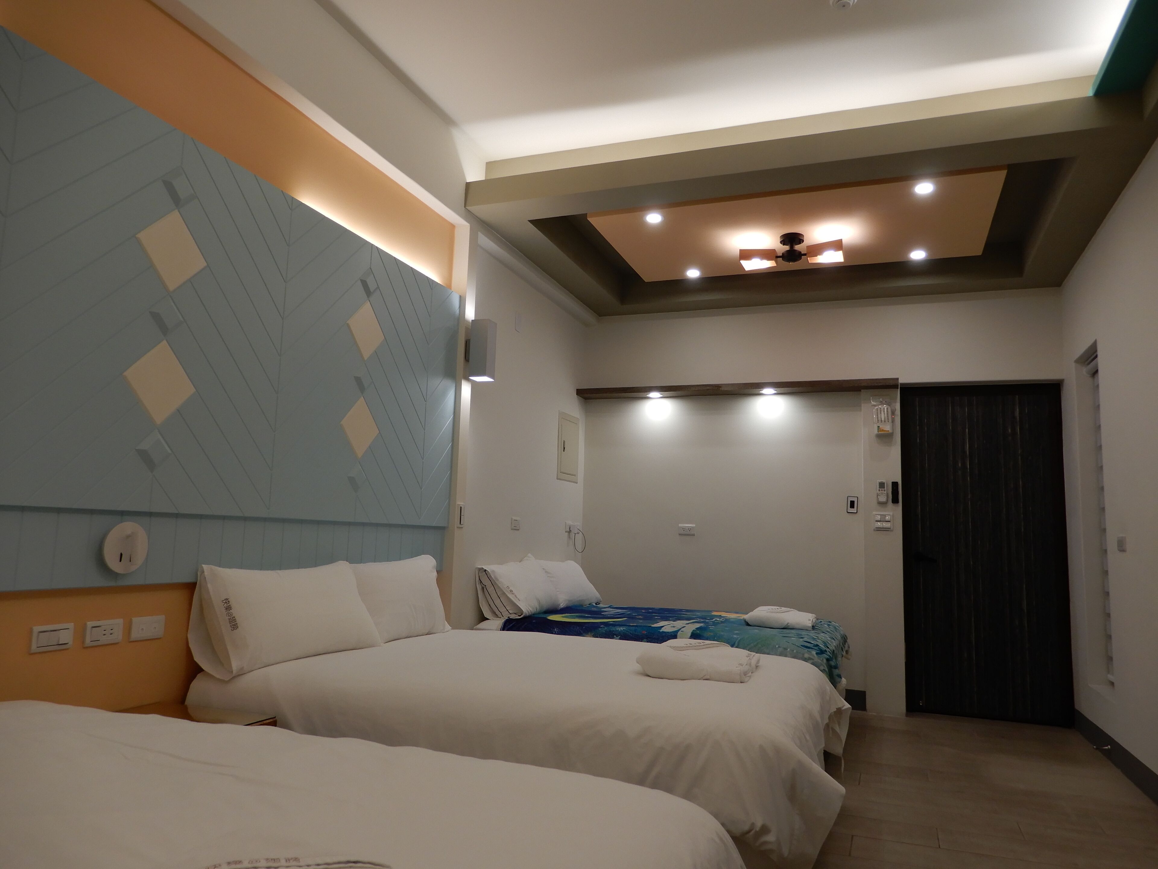 A hotel room with two beds, a ceiling fan, and a dark door.