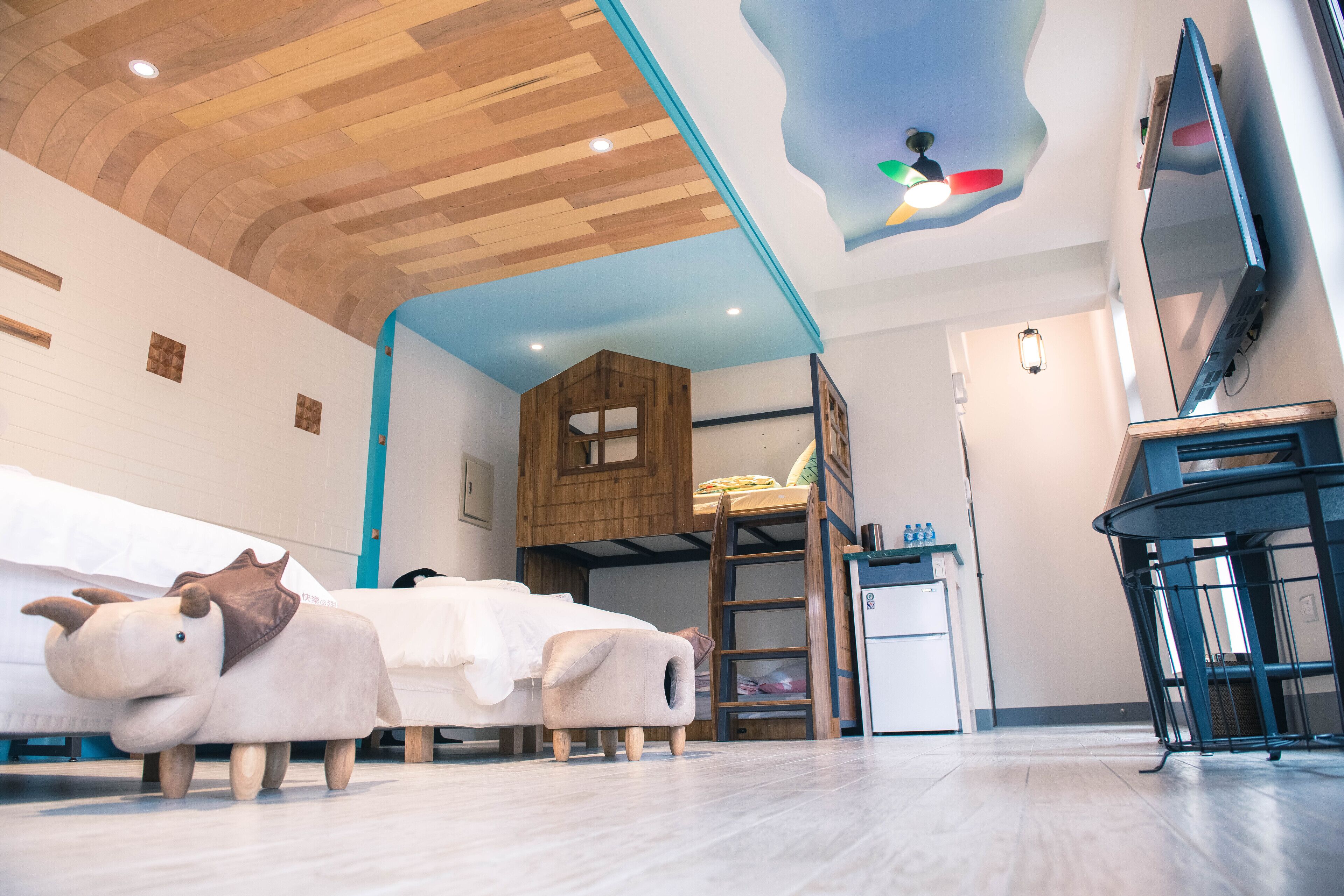 A room with a bunk bed, a small kitchenette, a wooden ceiling, and a ceiling fan.