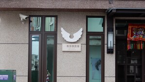 Fachada de edificio con una cámara de seguridad, un letrero con caracteres chinos y un emblema alado decorativo.