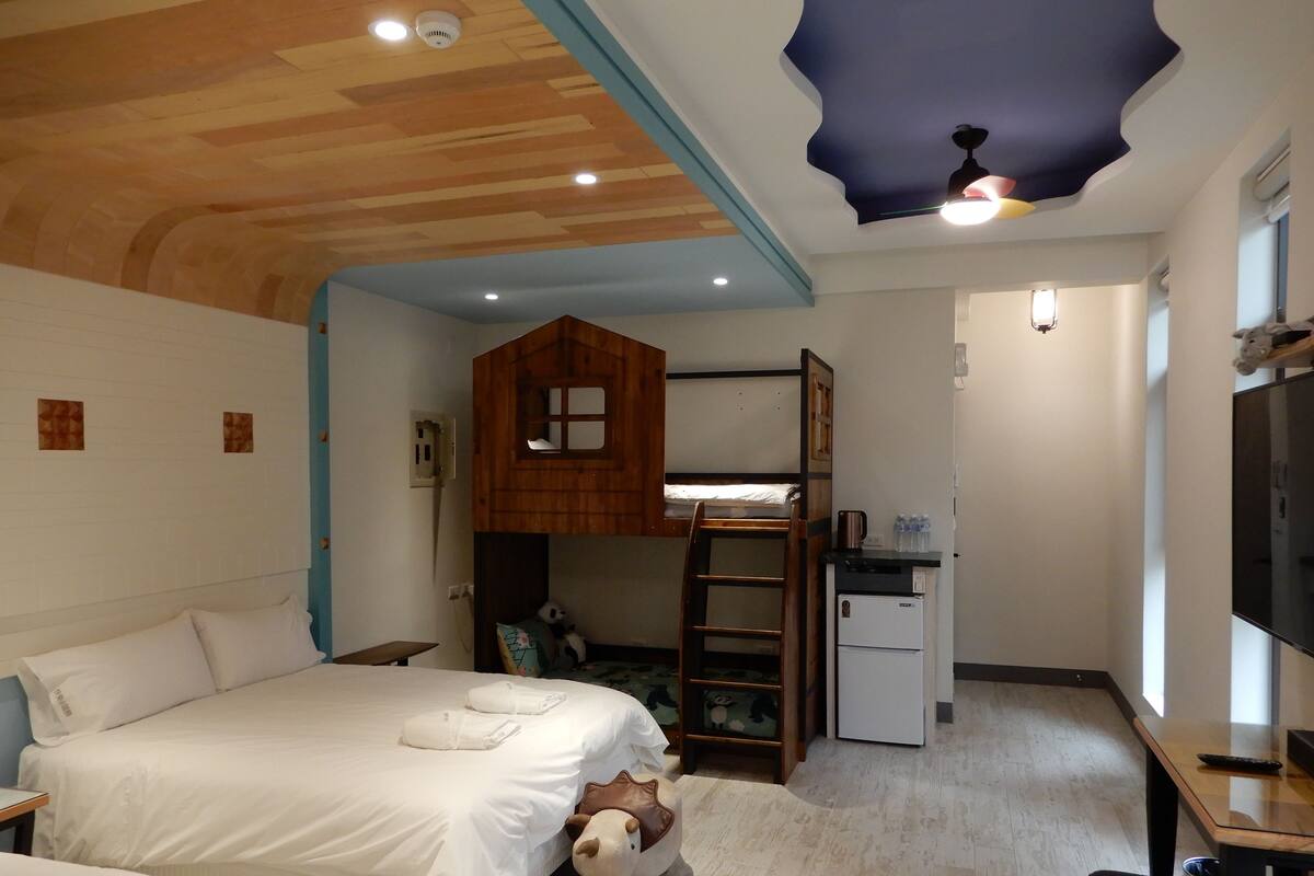 A bedroom with a bunk bed, a desk with a computer, a small refrigerator, and a television.