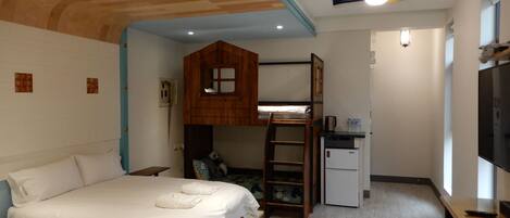 A bedroom with a bunk bed, a desk with a computer, a small refrigerator, and a television.