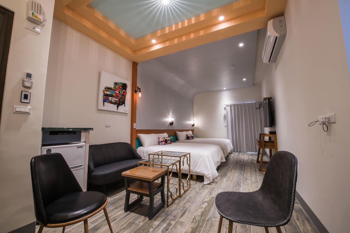 A hotel room with a bed, a sofa, a dining table, and a small kitchenette.