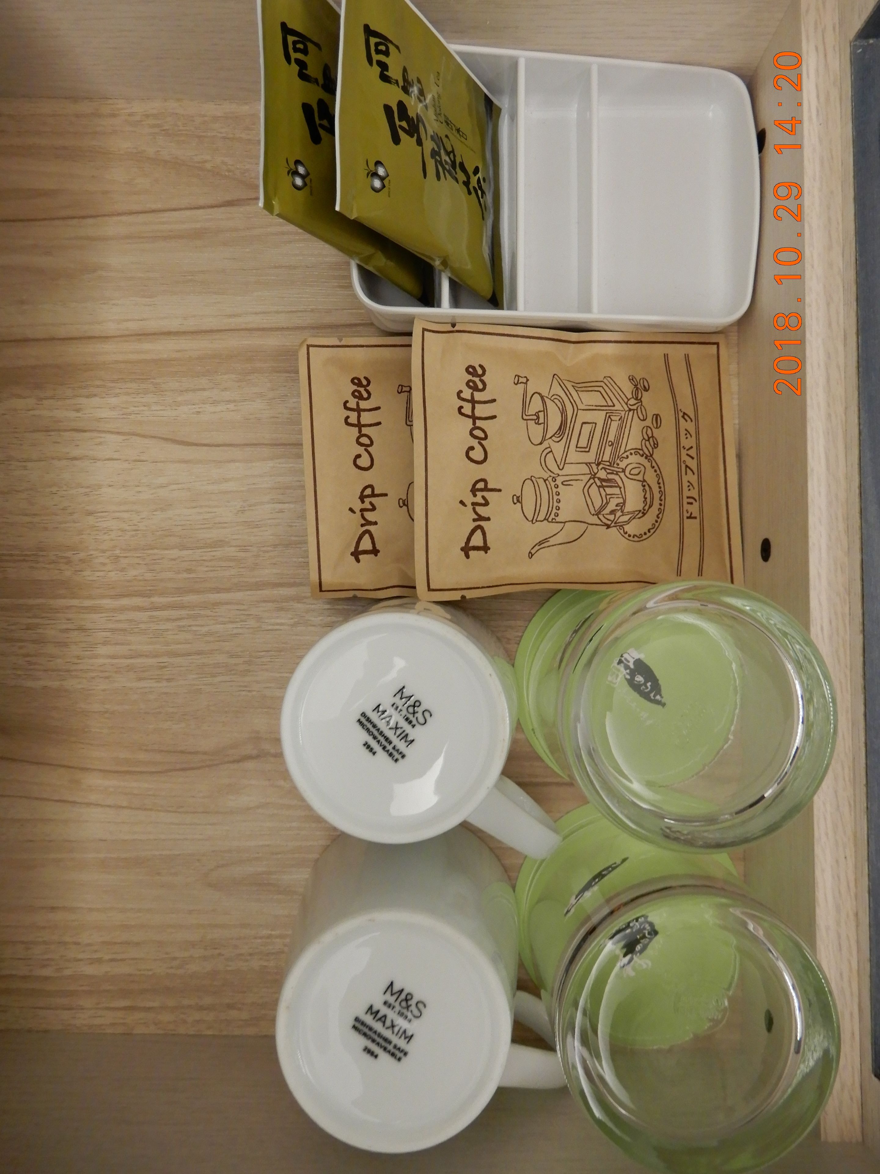 Una mesa de madera con dos tazas blancas, dos tazas verdes y dos sobres de café de filtro.