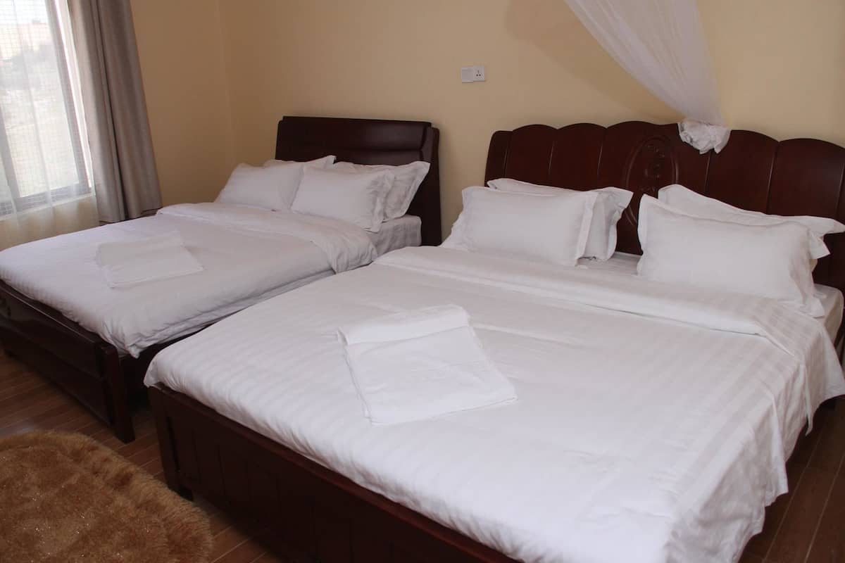Habitación de hotel con dos camas, cada una con ropa blanca y almohadas, cabecero de madera y dosel.