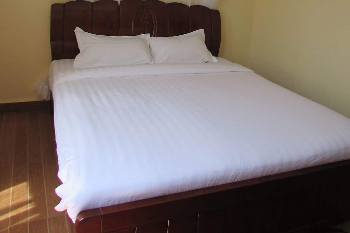 Una cama con sábanas blancas, cabecera de madera y dosel blanco.