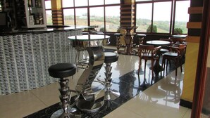 Una zona de bar con taburetes altos, una barra con botellas y grandes ventanales con vistas al exterior.
