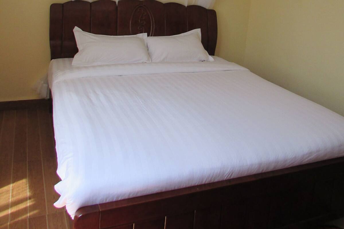 Una cama con dosel, cabecero de madera y ropa de cama blanca en una habitación con paredes amarillas.