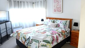 A bedroom with a bed, a desk, a nightstand, and a wall-mounted lamp. - CURNOWS BENDIGO RENTAL (Golden Square)