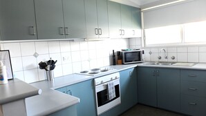 A modern kitchen with teal cabinets, a white countertop, a stove, a microwave, and a sink. - CURNOWS BENDIGO RENTAL (Golden Square)