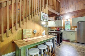 Interior de madera con barra, taburetes, refrigerador y encimera de cocina.