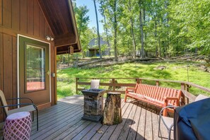 Une terrasse en bois avec des sièges d’extérieur, un foyer en pierre et une vue sur une zone boisée.