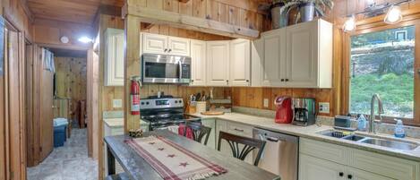 Cocina de cabaña de madera con estufa, microondas, pileta y alacenas.