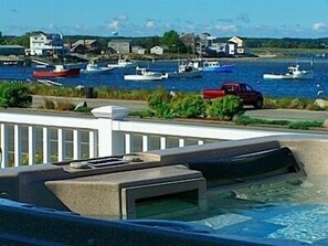 Vista de un puerto deportivo con barcos amarrados, una camioneta roja en la orilla y casas al fondo.