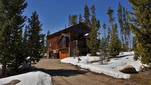 Une cabane en rondins dotée d’une grande véranda et de nombreuses fenêtres, entourée de neige et de pins.