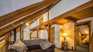Acogedor dormitorio en ático con sofá seccional marrón, vigas de madera y una pequeña mesa con lámpara.