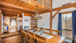 Una mesa de comedor de madera con sillas, una araña y una ventana con cortinas.