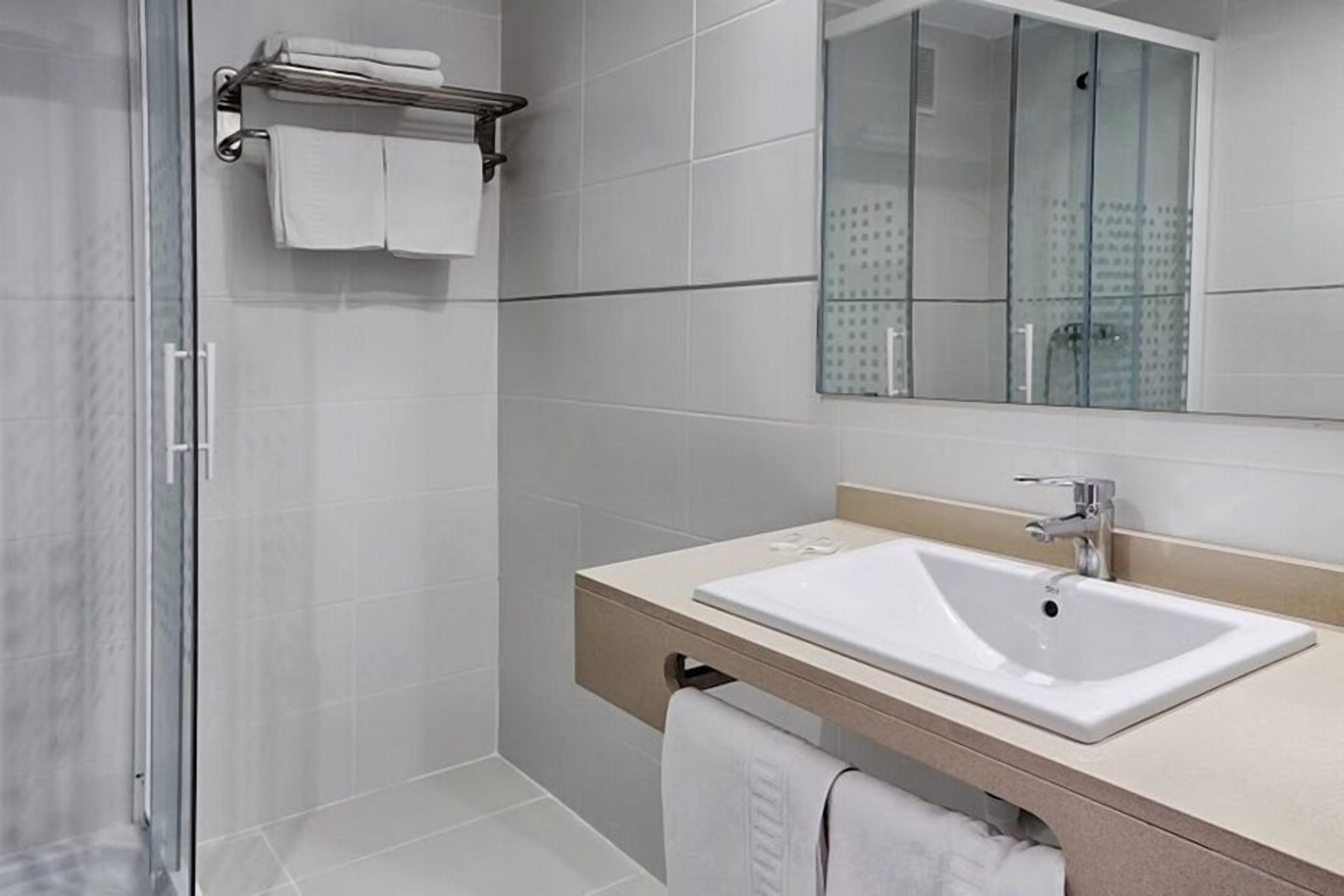 Une salle de bain moderne avec une douche à l’italienne en verre, un lavabo blanc et un grand miroir.