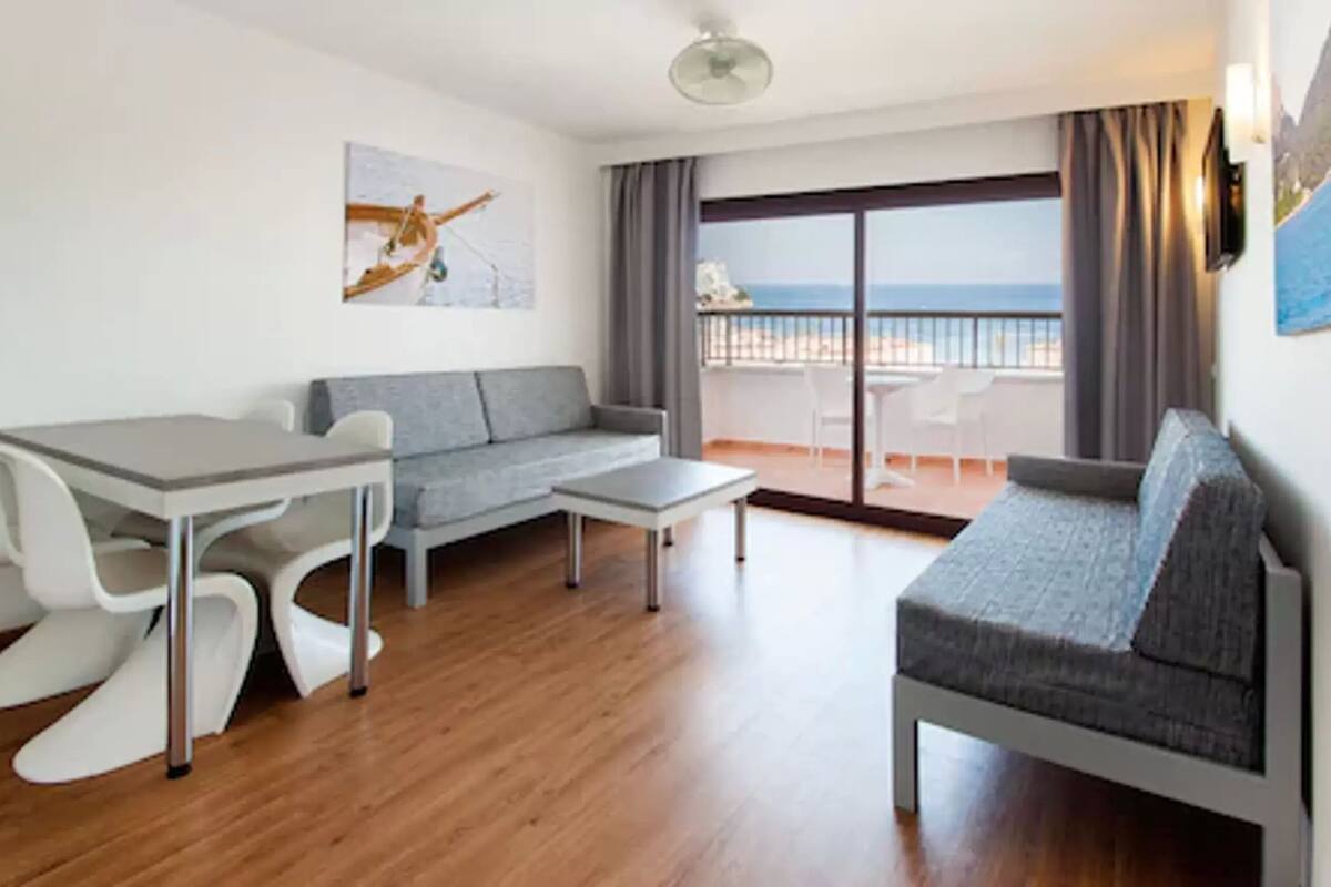 Una sala de estar moderna con una mesa de comedor, dos sofás y un balcón con vistas al mar.