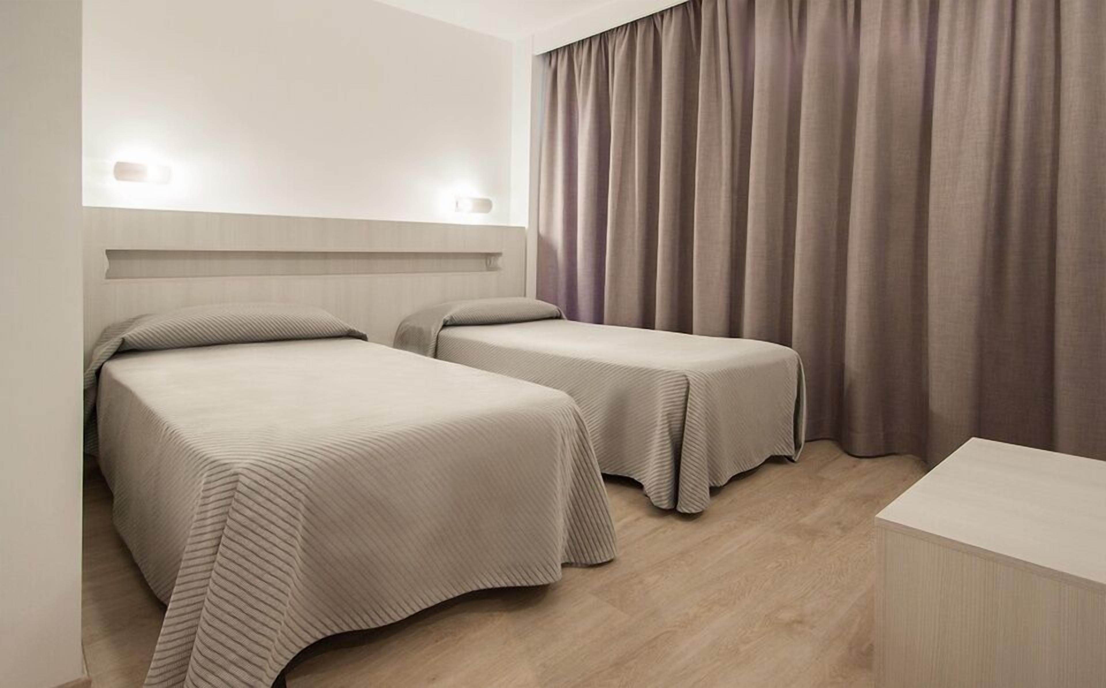 A hotel room with two beds, a headboard, a bedside table, and a curtain.