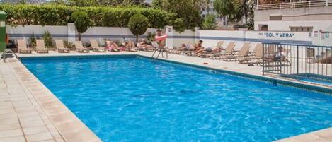 Une piscine avec des chaises longues et un panneau indiquant « SOL Y VERA ».