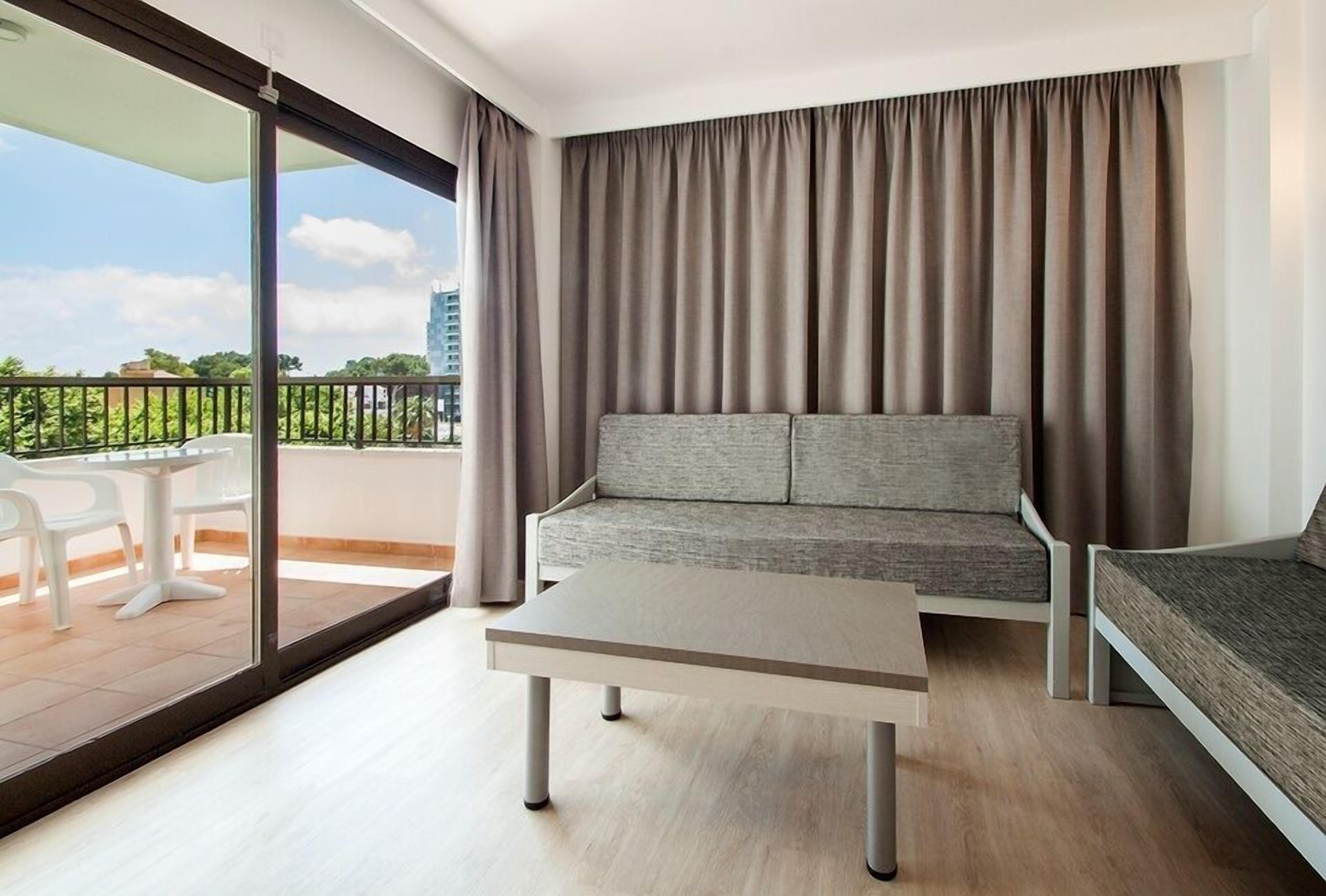 Un salón moderno con sofá, una mesa de centro y un balcón con vistas a zonas verdes y edificios.