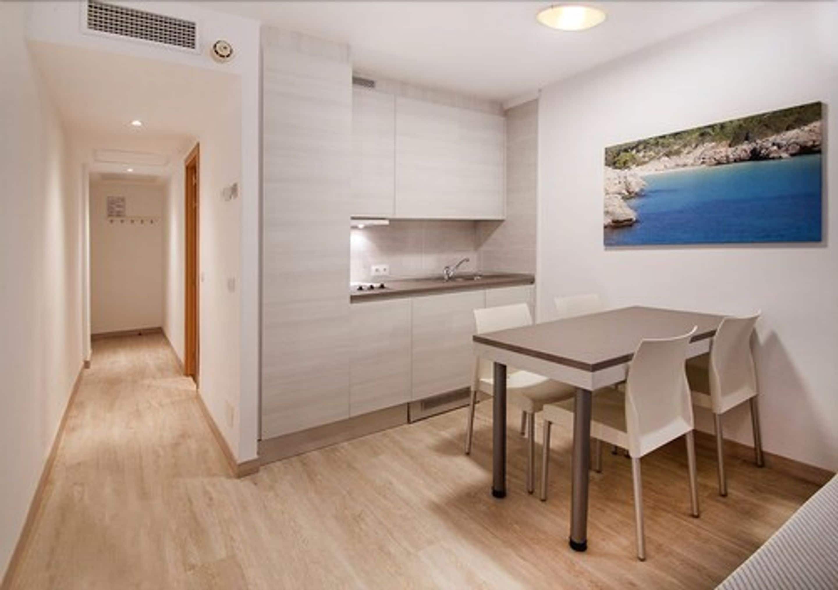 A modern kitchen with white cabinets, a dining table with chairs, and a painting of a coastal scene on the wall.