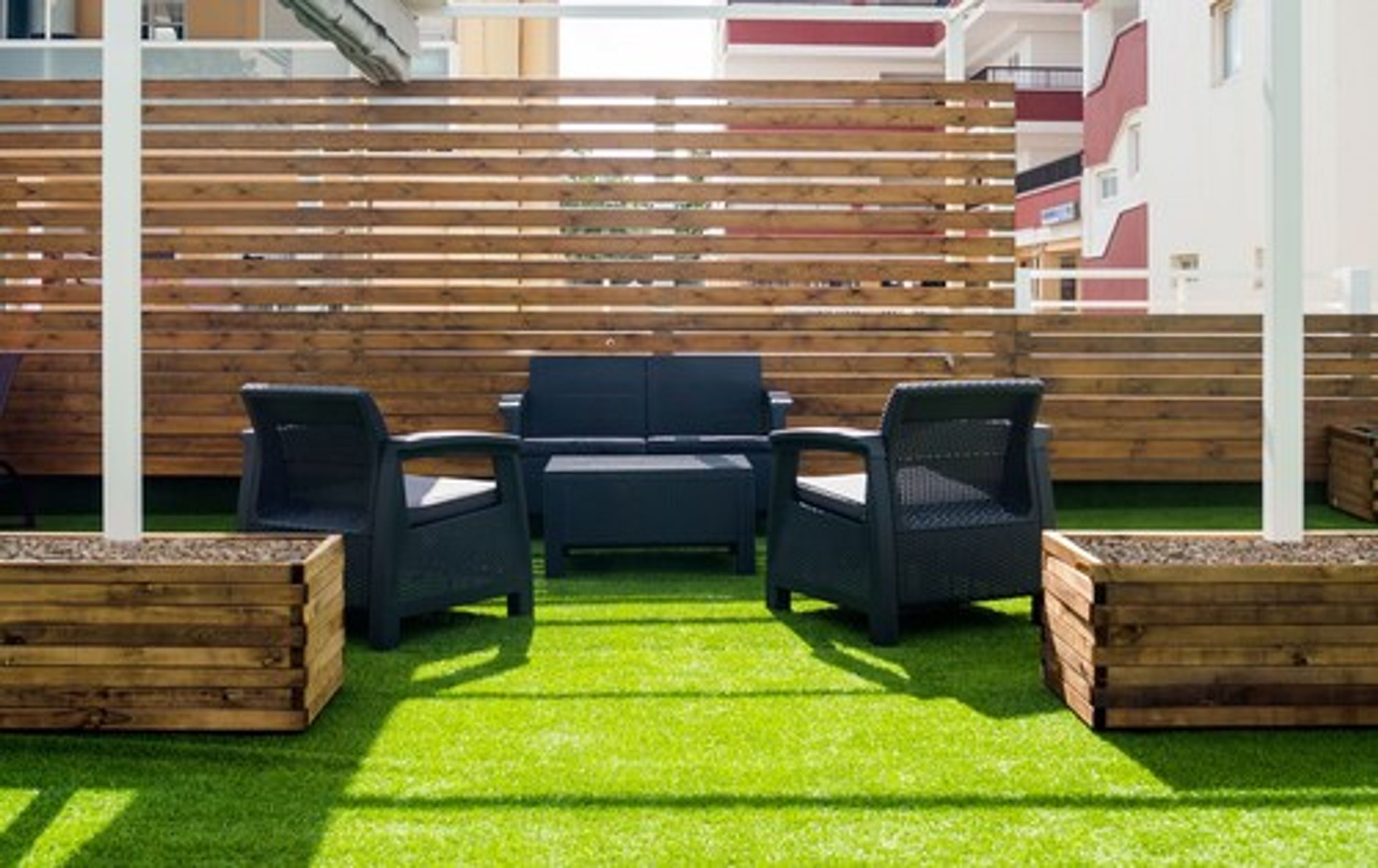 A patio area with a wooden fence, green artificial grass, and a seating arrangement of two chairs and a table.