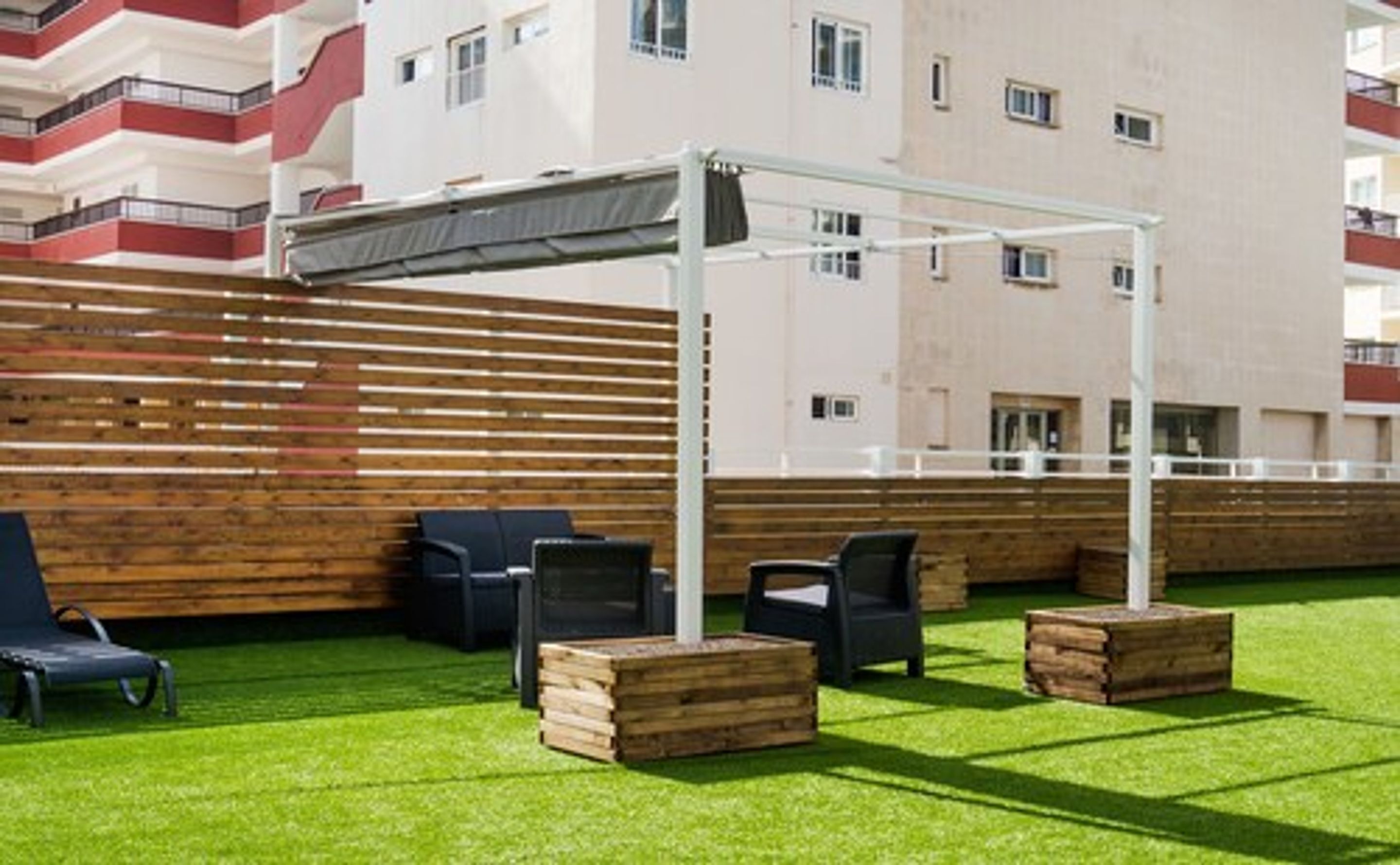 An outdoor seating area with a pergola, wooden benches, and artificial grass.