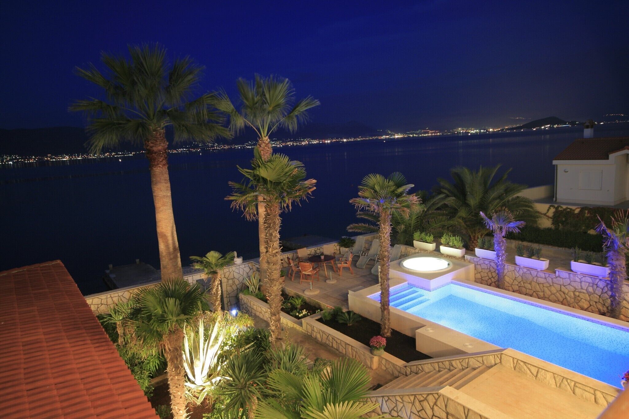 A nighttime view of a pool area with palm trees, a hot tub, and a stone wall.