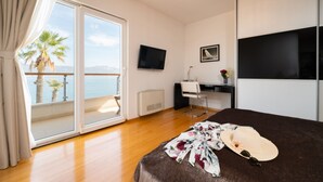 Ein Hotelzimmer mit Bett, Schreibtisch, Fernseher und einem Balkon mit Blick auf Palmen und das Meer.