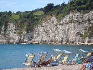 A beach with white cliffs in the background and several striped beach chairs. - Ideal for families, quiet spot, 4 min walk to beach, village, pubs, restaurants. (Beer)