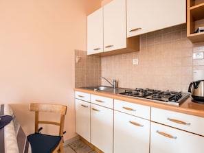 Een kleine keuken met witte kastjes, een gasfornuis en een spoelbak.