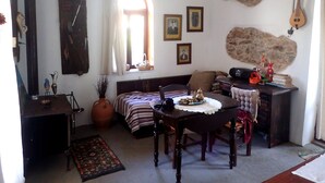 Ett mysigt vardagsrum med en soffa i trä, ett matbord med stolar, ett stort fönster med gardiner och en vägg av sten med en gitarr.