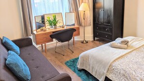 Un dormitorio con cama, escritorio, silla, armario y ventana con cortinas.