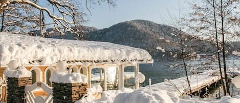 A snow-covered cabin with a stone foundation, wooden beams, and a glass door.