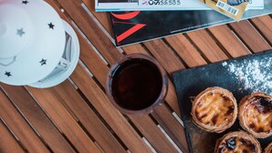 A table with a magazine, a glass of dark liquid, a white lamp, and pastries.