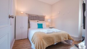 A bedroom with a bed, a wardrobe, a nightstand, and a lamp.