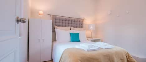 A bedroom with a bed, a wardrobe, a nightstand, and a lamp.
