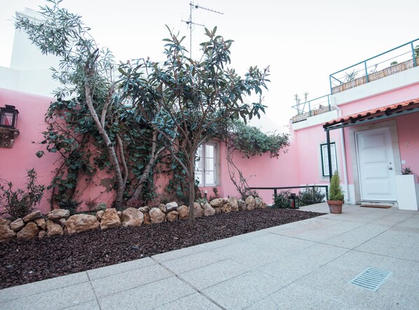 Um edifício rosa com uma parede de pedra e uma árvore ao primeiro plano.