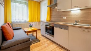 Eine kleine Küche mit Einbauofen, Geschirrspüler und Spüle. Es gibt eine Holz Arbeitsplatte und ein Fenster mit gelben Vorhängen.
