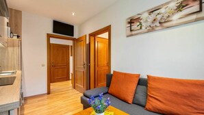 Ein modernes Wohnzimmer mit einem grauen Sofa, orangefarbenen Kissen, einem Couchtisch aus Holz mit einer Pflanze und einem Gemälde an der Wand.