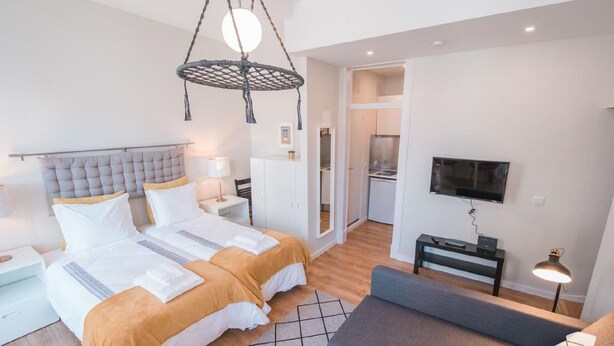 A modern hotel room with a double bed, bedside tables, a TV, and a hanging light fixture.
